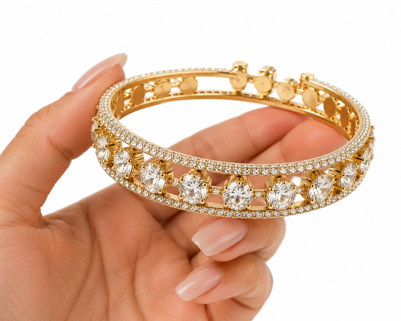 A gold bangle bracelet with pavé-set clear stones and large round center stones, held in a hand against a white background.