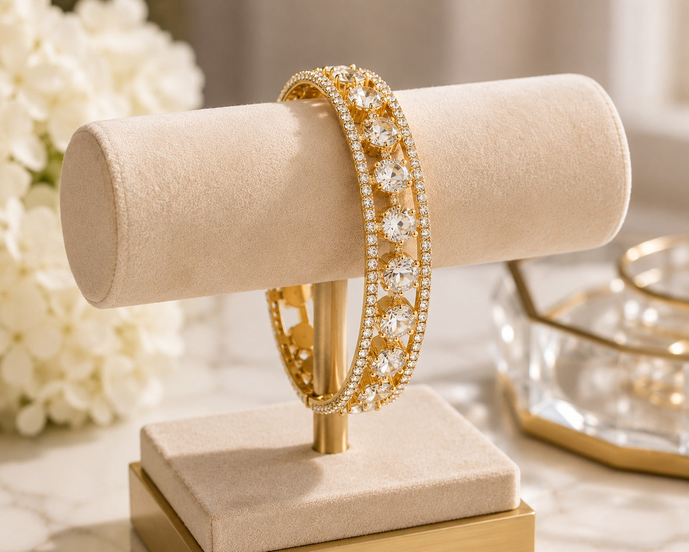 A gold bangle bracelet with pavé-set clear stones, displayed on a beige jewelry stand with a soft, elegant background.