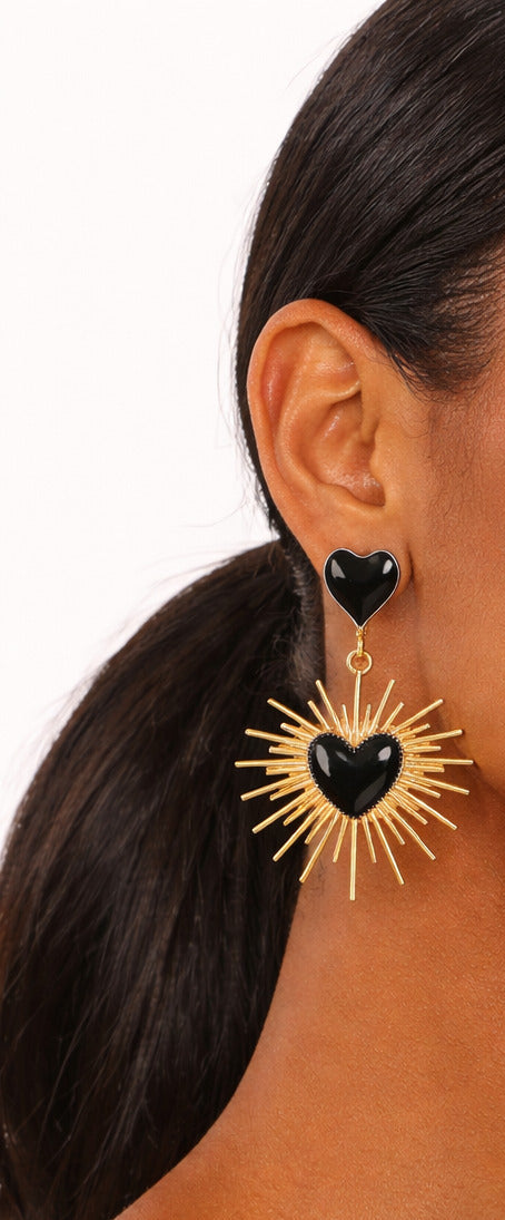 Woman wearing large hoop earrings with black heart centers on a white background