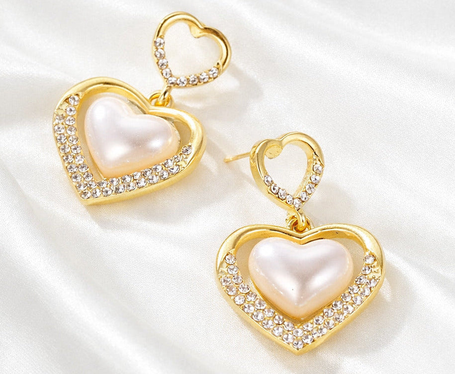 Heart-shaped earrings with gold frames and pearl centers on a white background
