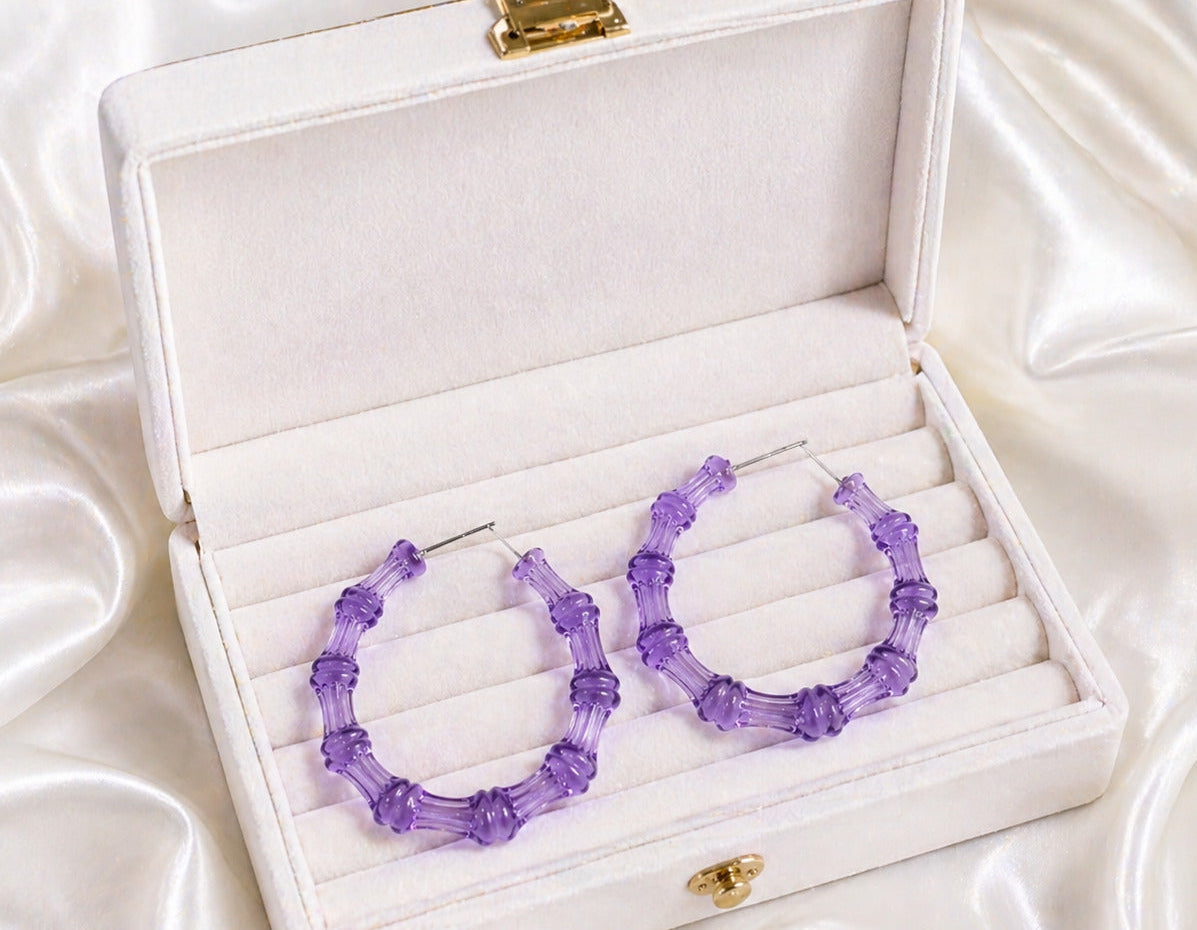 Purple hoop earrings in a white jewelry box on a satin surface