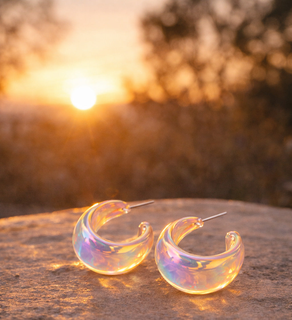 Iridescent hoop earrings on a textured surface with a sunset background