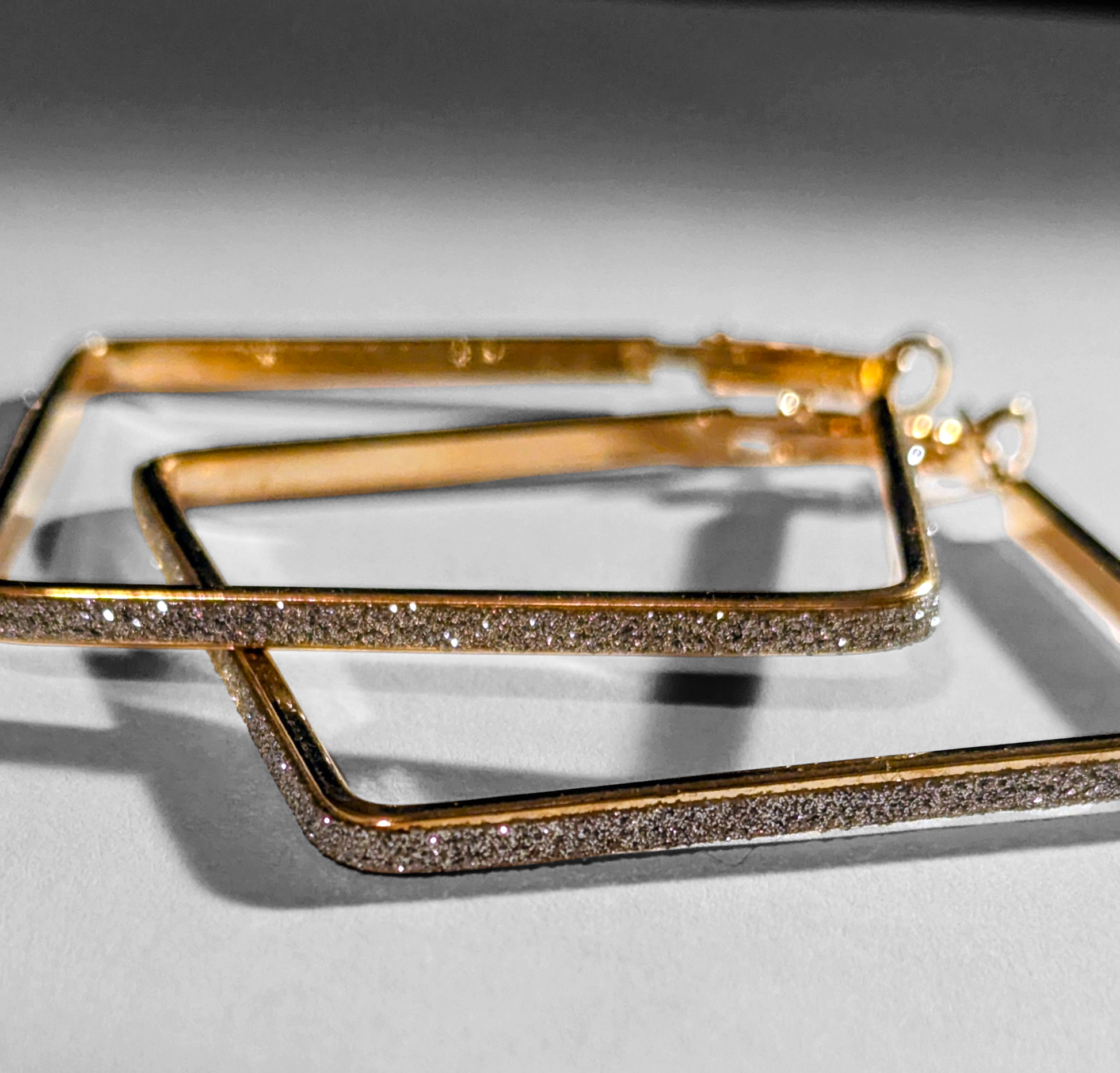 Gold hoop earrings with diamond-like stones on a light gray background