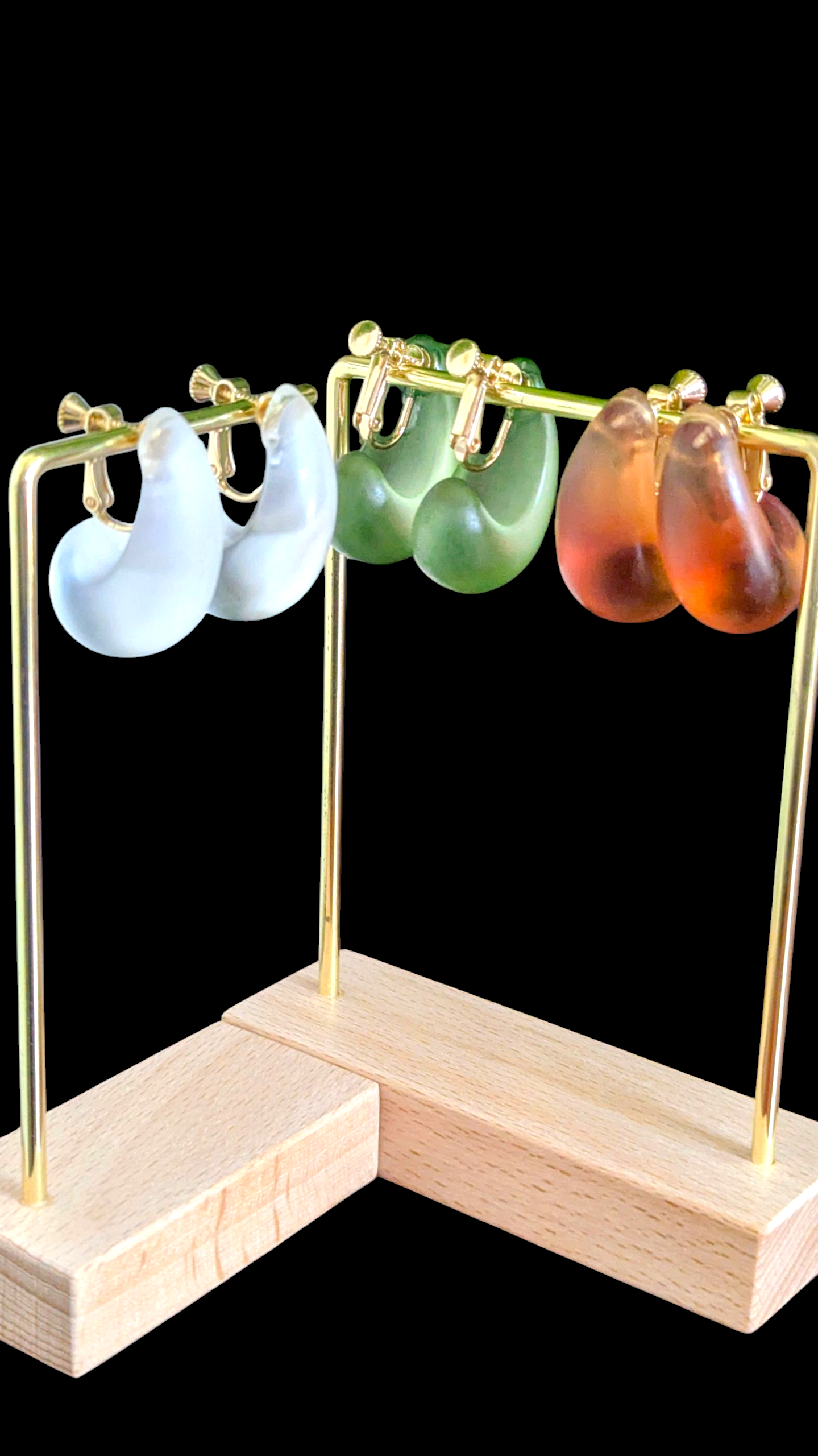 Set of colorful earrings on a wooden stand against a black background