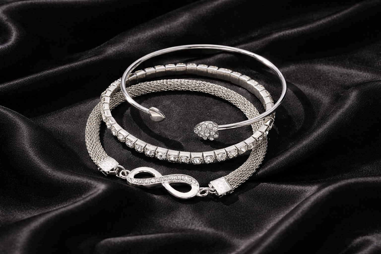 Silver bracelets with intricate designs on a black satin background