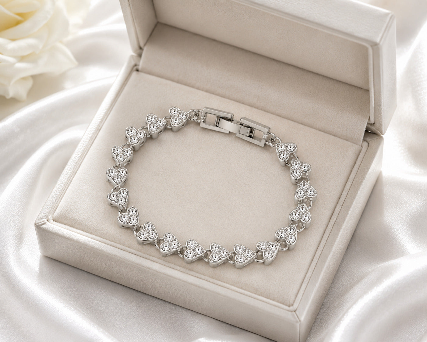 A silver-toned heart-link bracelet displayed inside an open cream jewelry box on a white satin fabric background.