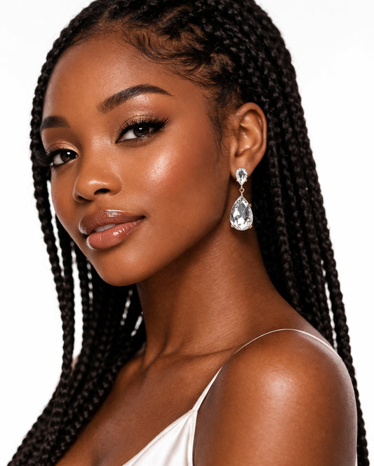 Woman with braided hair wearing a white top and teardrop earrings on a plain background