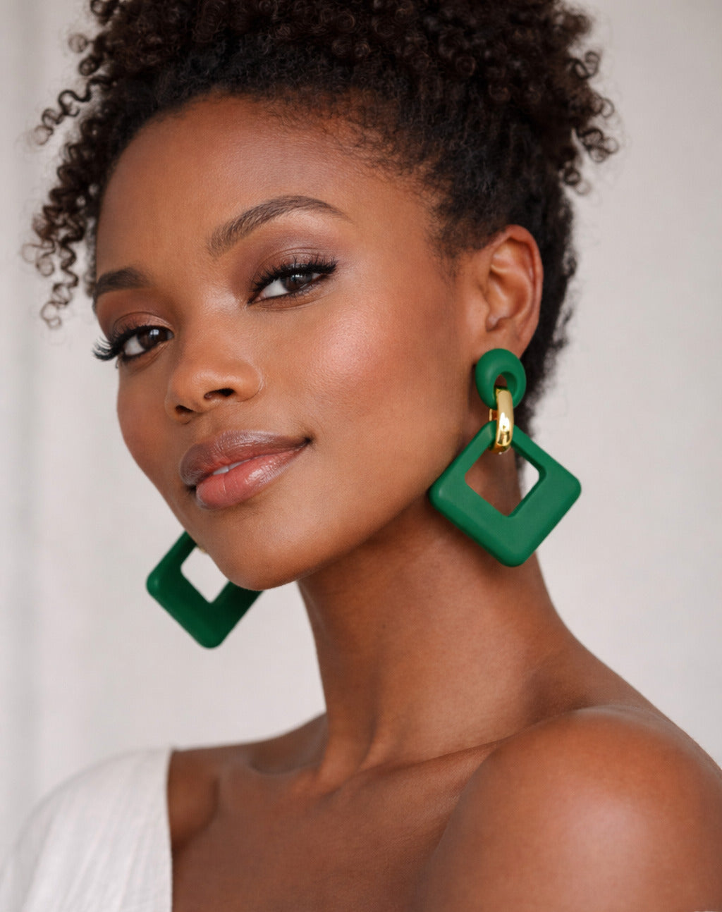 Woman wearing green square earrings against a white background