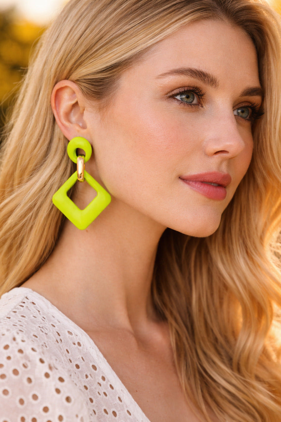 Woman wearing bright green earrings with a blurred natural background