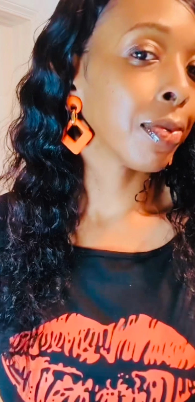 A person wearing the velvet rhombus drop earrings with a gold clip attachment, showcasing the earrings in an orange and black color.
