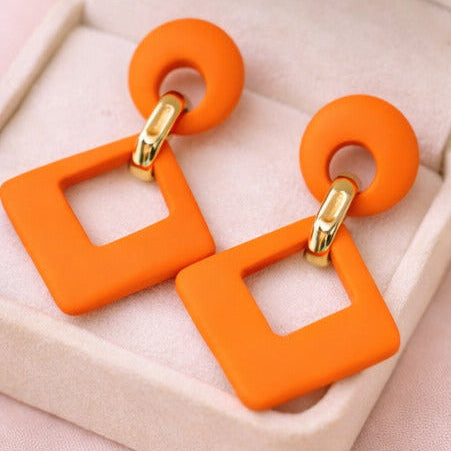 Orange square-shaped earrings with gold accents on a jewelry box and a vanity table.