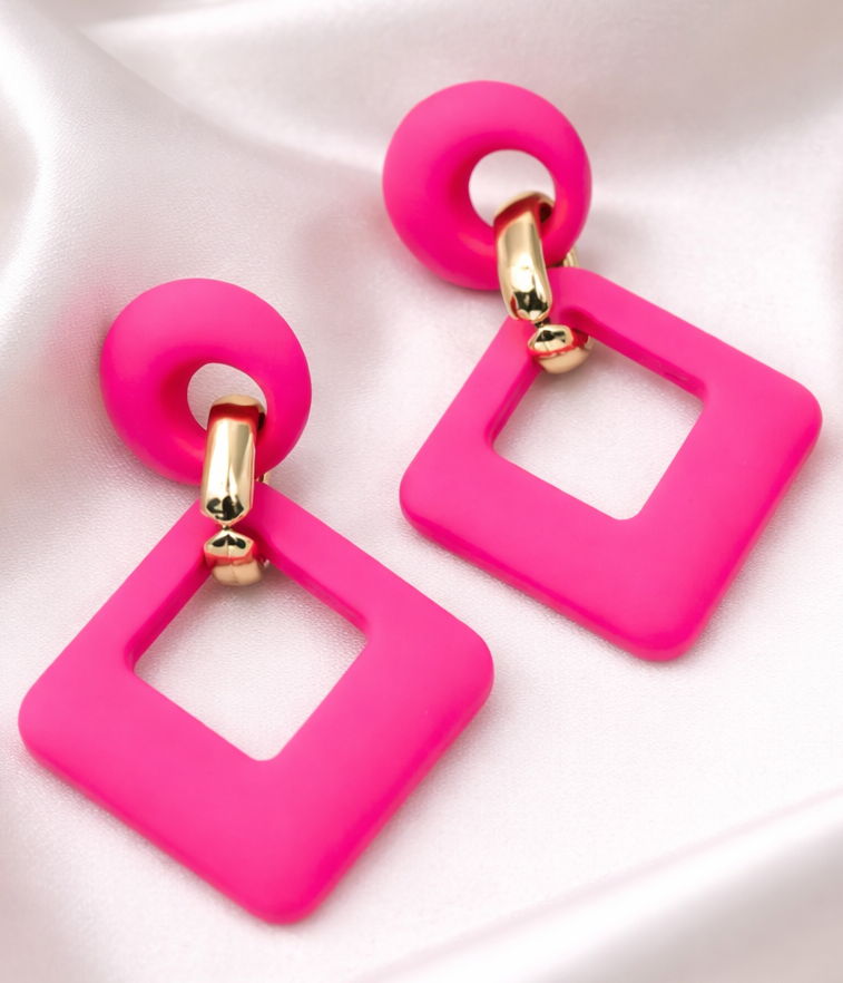 Pink square earrings with gold accents on a white fabric background