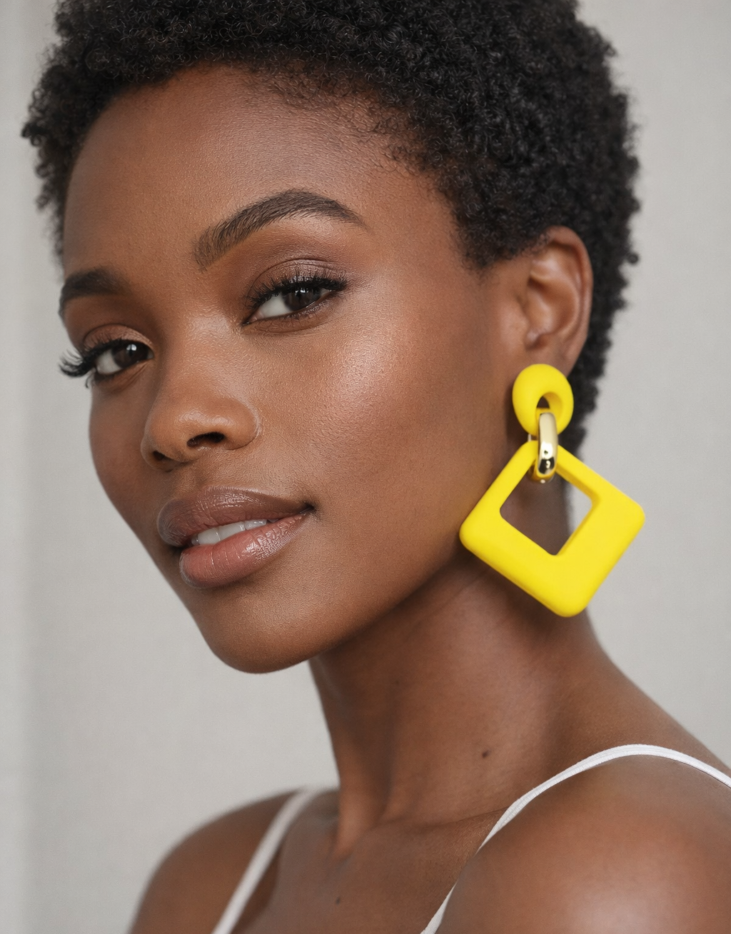 Woman wearing bright yellow square earrings against a neutral background